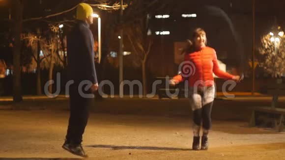 与户外私人教练一起健身年轻迷人的女人晚上在公园里跳绳男教练视频的预览图