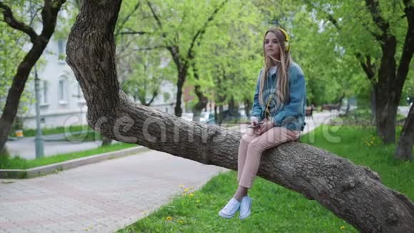 女人坐在公园的一棵树上听音乐视频的预览图