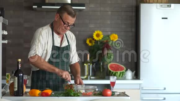戴眼镜的成熟男人在厨房准备沙拉把蔬菜放在碗里搅拌带着严肃的面孔退休视频的预览图