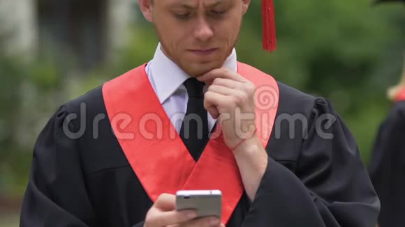 认真的男毕业生揉着下巴看着智能手机收到好消息视频的预览图