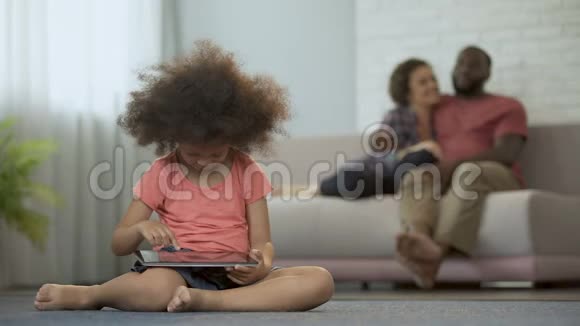 年轻的父母享受着共同的消遣看着他们的女儿在平板电脑上玩视频的预览图