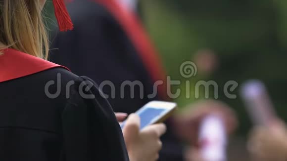 女大学毕业生在智能手机上打字和发送信息的背面视图视频的预览图