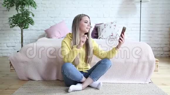 漂亮的年轻女人在家坐在地板上打电话视频的预览图