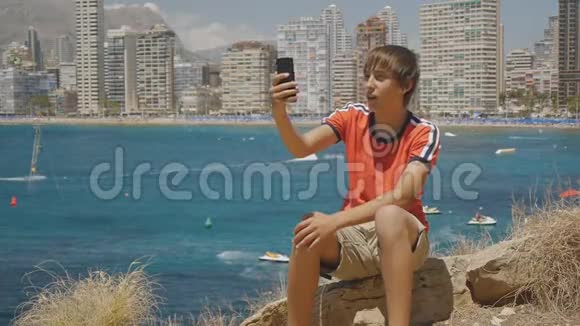 白种人少年用智能手机进行视频通话显示海上海岸和摩天大楼的轮廓视频的预览图