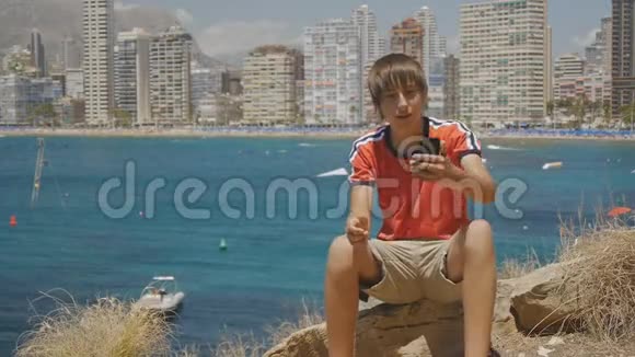 白人青少年开始视频通话智能手机在海上海岸和摩天大楼天际线背景视频的预览图