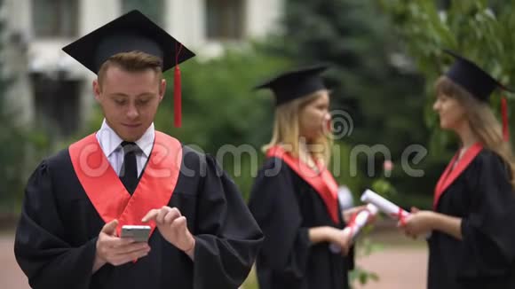 毕业日年轻人浏览智能手机微笑着寻找相机视频的预览图