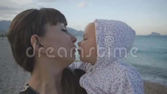 年轻的母亲带着孩子在日落海滩上性感的白种人女人用空吻两岁小孩视频的预览图