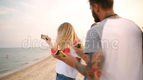 朋友吃西瓜站在沙滩上用智能手机相机自拍穿着视频的预览图