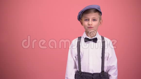 穿着老式衣服的小男孩看着摄像机被隔离在粉红色的背景上视频的预览图