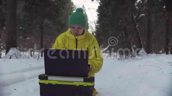 在冬季森林里的笔记本电脑上工作的运动服装生态学家视频的预览图