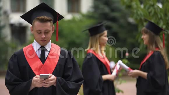男毕业生用手机打字用相机微笑毕业视频的预览图