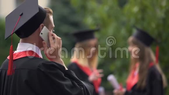 快乐的男毕业生在智能手机上交谈微笑着毕业日视频的预览图