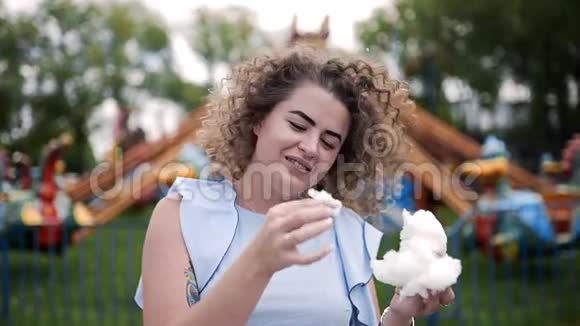 夏天一位留着卷发的美女在游乐园吃棉花糖和微笑视频的预览图