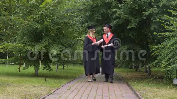 年轻的快乐毕业生拿着文凭在公园里散步聊天放松视频的预览图