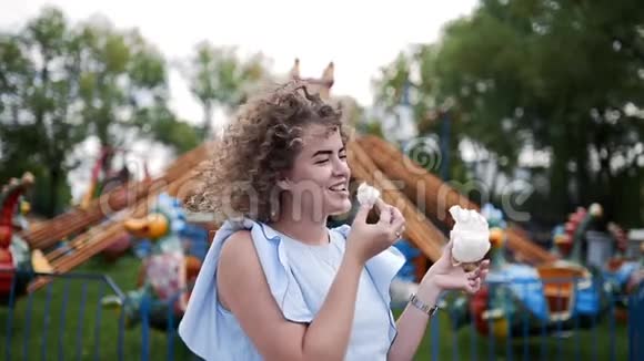 夏天一位留着卷发的美女在游乐园吃棉花糖和微笑视频的预览图