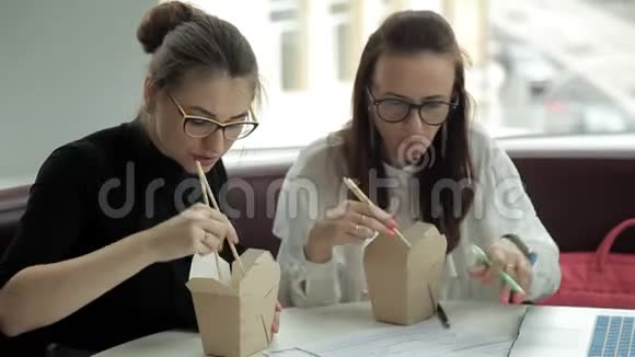 两个年轻的商业女孩坐在咖啡馆里吃中国面条讨论商业发展工作吃东西视频的预览图