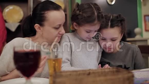 漂亮的妈妈和两个女儿在咖啡馆里用电话笑视频的预览图