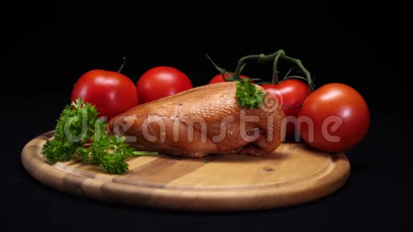 黑色背景的木板上躺着烤鸡西红柿和青菜的特写镜头框架视频的预览图