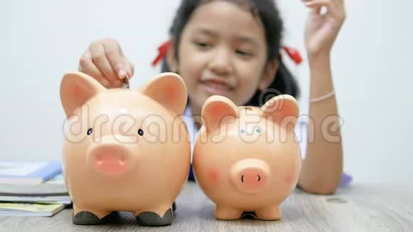 穿着泰国学生制服的亚洲小女孩把硬币放在猪的储蓄罐里浅浅的田野选择聚焦在猪身上视频的预览图