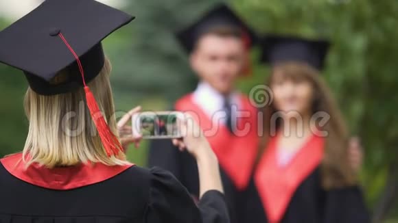 女学生穿着学术服装戴着帽子通过电话拍摄最好的朋友毕业日视频的预览图