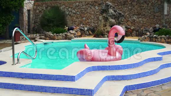 粉红色的火烈鸟橡胶圈在雨中漂浮在游泳池里视频的预览图