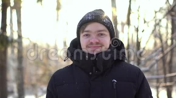 年轻的微笑的男人在冬日的树林里阳光明媚穿着冬装的快乐男人微笑着直视着金色视频的预览图