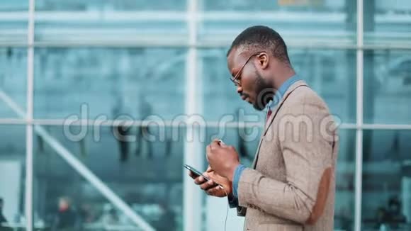 非裔美国商人一边听音乐一边跳舞一边拿着智能手机在办公楼附近散步视频的预览图