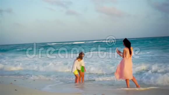 温暖的夜晚可爱的小女孩和年轻的母亲在热带海滩妈妈拍了一张漂亮孩子的照片视频的预览图