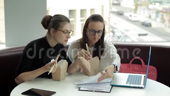 两个年轻的商业女孩坐在咖啡馆里吃中国面条讨论商业发展工作吃东西视频的预览图