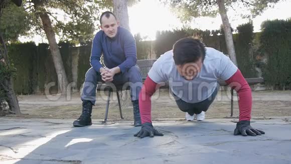 与户外私人教练一起健身男性运动员在公园里做超级慢俯卧撑作为锻炼常规的一部分视频的预览图