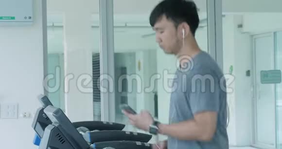 带着耳机在健身房跑步机上跑步的亚洲年轻人视频的预览图