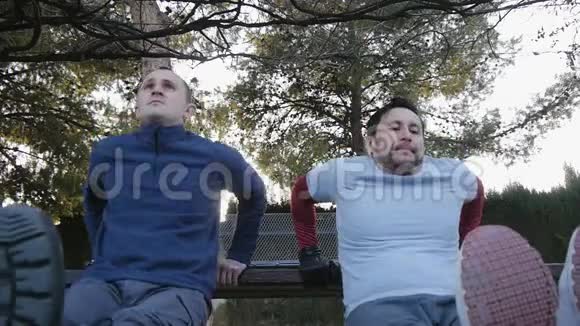 与户外私人教练一起健身作为公园的一部分两名健身男子在公园里做三头肌长凳视频的预览图