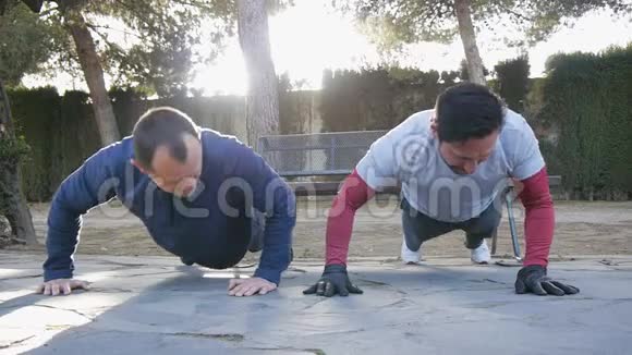与户外私人教练一起健身两名男性运动员同时在一个公园里做俯卧撑作为一个公园的一部分视频的预览图