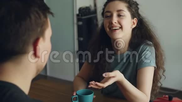 年轻的白种人夫妇坐在现代厨房的餐桌前正以积极的方式讨论一些事情而男人则坐在后面视频的预览图