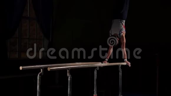 在黑暗的房间里男体操运动员在双杠上缓慢地表演倒立视频的预览图