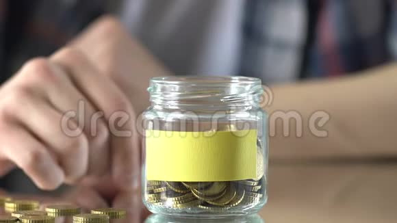 男人把钱存在玻璃罐里空贴纸作为笔记为梦想投资视频的预览图