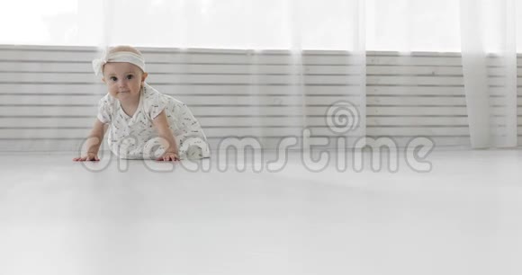 一个穿着绷带和裙子的漂亮小女孩在白色的地板上爬行视频的预览图