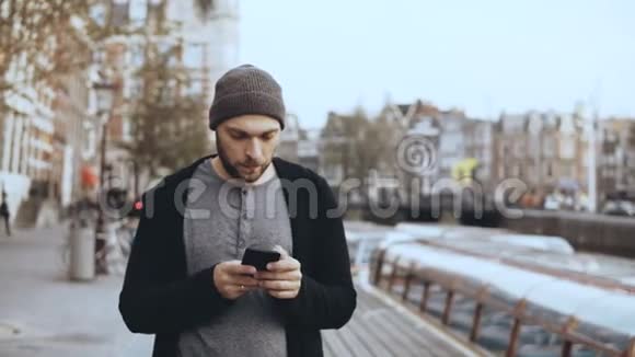 4K休闲集中的人使用智能手机英俊的胡子创意欧洲男性戴帽子在街上发短信视频的预览图