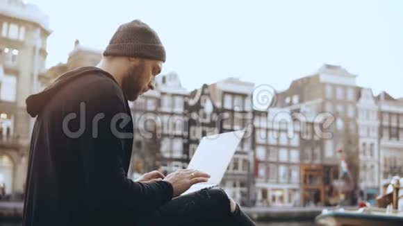 4K创意人坐在街上拿着笔记本电脑工作移动办公室阿姆斯特丹老城区大气城市景观视频的预览图