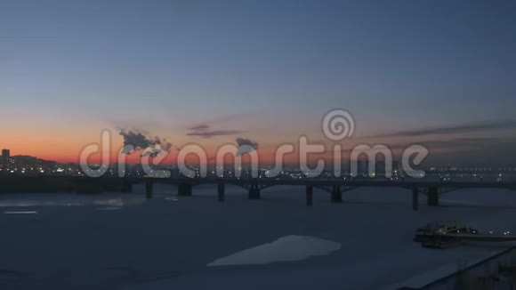 空中无人机观雪覆盖的夜城冬天冰封的河流红日落视频的预览图