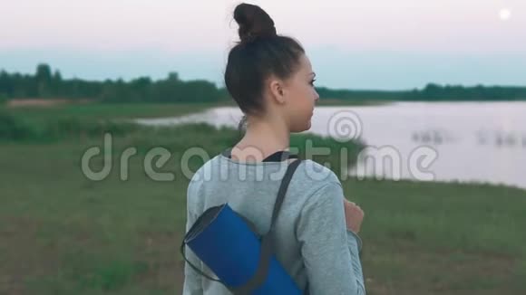 女孩拿着蓝色的瑜伽垫年轻女子走路做晨练瑜伽视频的预览图