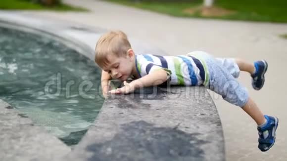 4k镜头可爱的幼儿男孩在公园的喷泉里摸水视频的预览图