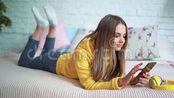 美丽的女孩在床上听耳机音乐用电话放松视频的预览图