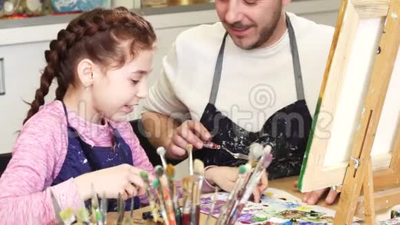一个可爱的小女孩微笑着和她爸爸在美术课上混合颜料的不规则镜头视频的预览图