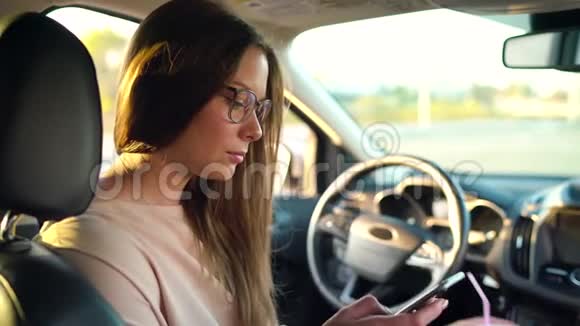 戴眼镜的女人在智能手机上说话在车里喝咖啡视频的预览图