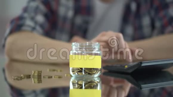 男人计算开支把钱放进装有空贴纸的玻璃罐里视频的预览图