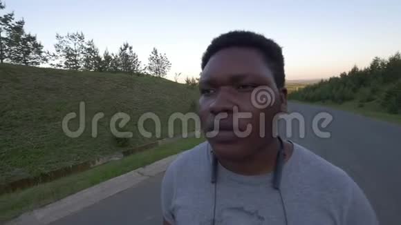 年轻的非裔美国人走在空荡荡的路上在夕阳下抽烟视频的预览图
