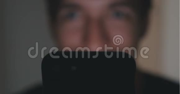 在家里的飞镖室用智能手机关闭年轻人他脸上的智能手机反射视频的预览图