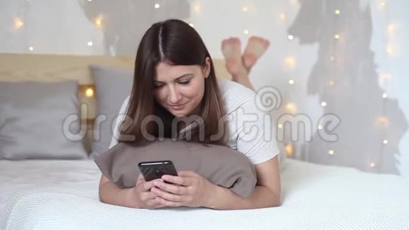 美丽的女孩喜欢躺在床上的手机心情很好视频的预览图