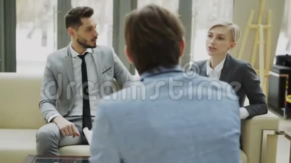 在现代的办公室里女商人与坐在沙发上的男商人交谈和嘲笑的镜头视频的预览图